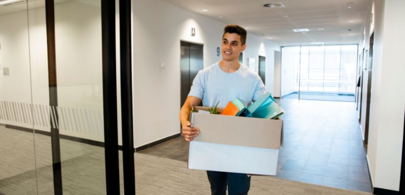Ein neuer Mitarbeiter trägt eine Box mit verschiedenen Arbeitsmaterial in ein Büro.