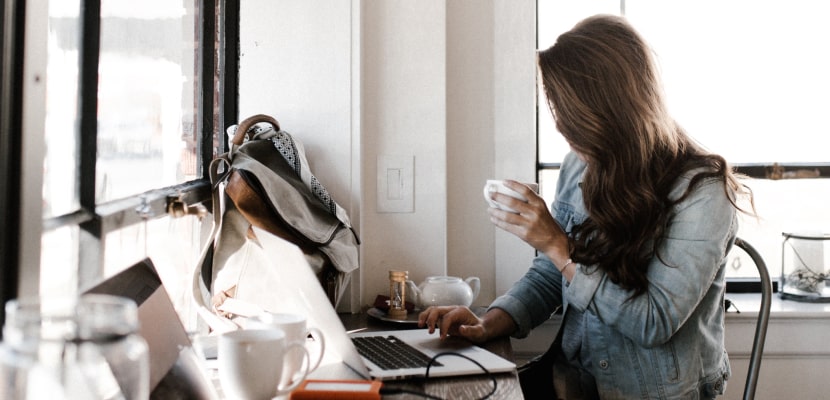 Eine Frau sitzt mit Kaffee vor ihrem Laptop und startet mit Achtsamkeit in ihren Arbeitstag.