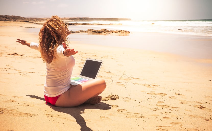 Eine digitale Nomadin arbeitet mit ihrem Laptop am Strand.