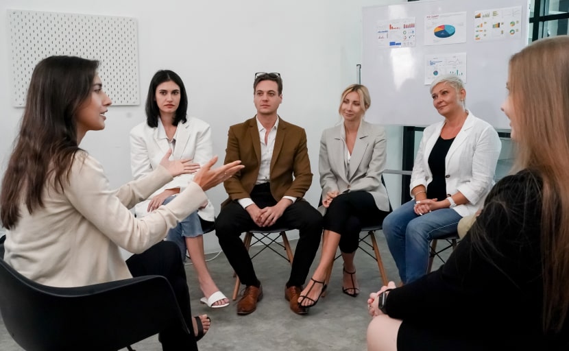 Mitarbeitende sitzen im Kreis zu einem Meeting zusammen.
