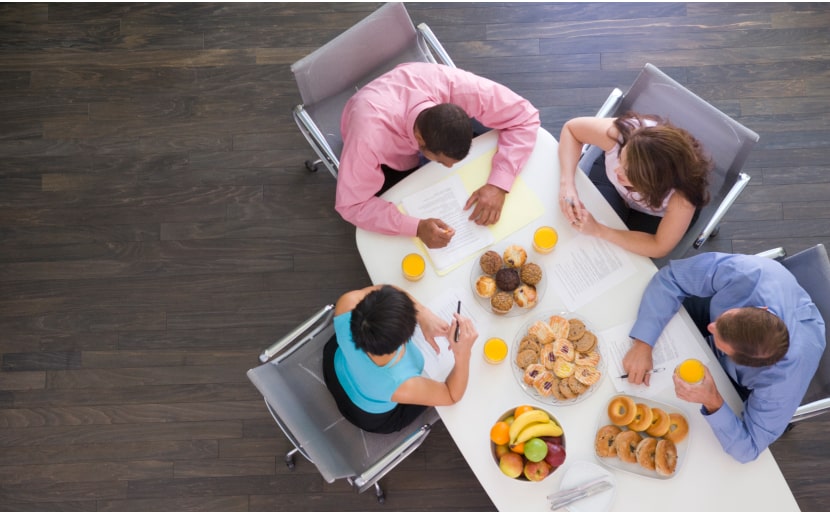 Mitarbeitende sitzen mit Frühstück als Sachbezugswert an einem Tisch im Büro und essen.