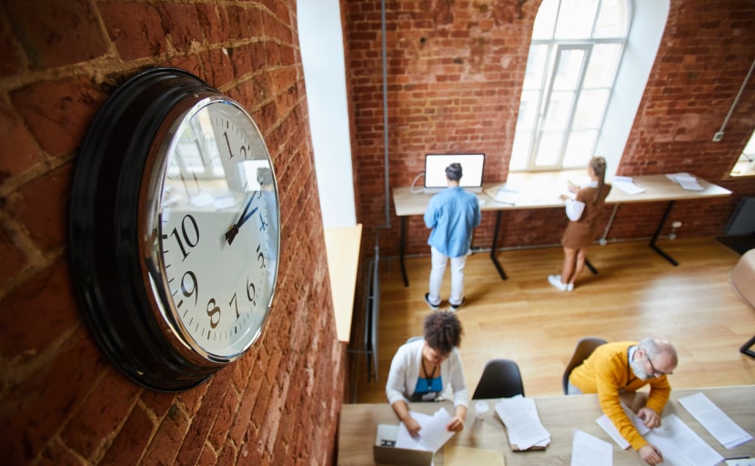 Mitarbeitende arbeiten in einem Büro mit einer Uhr an der Wand.