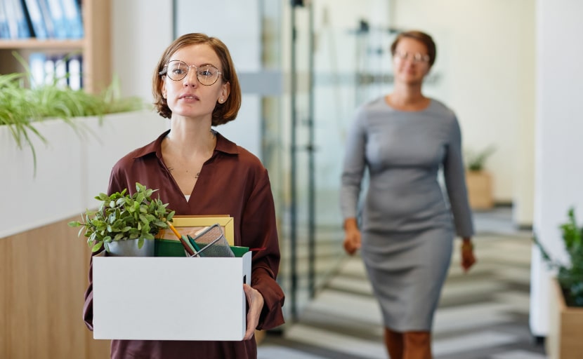 Eine Frau verlässt nach einer fristlosen Kündigung das Büro mit einer Box mit ihren persönlichen Gegenständen.