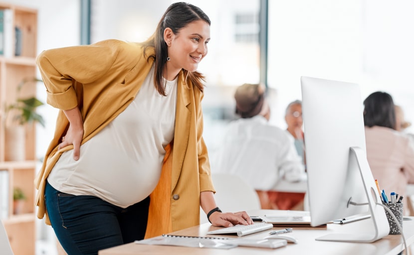 Eine schwangere Mitarbeiterin steht vor ihrem Computer.